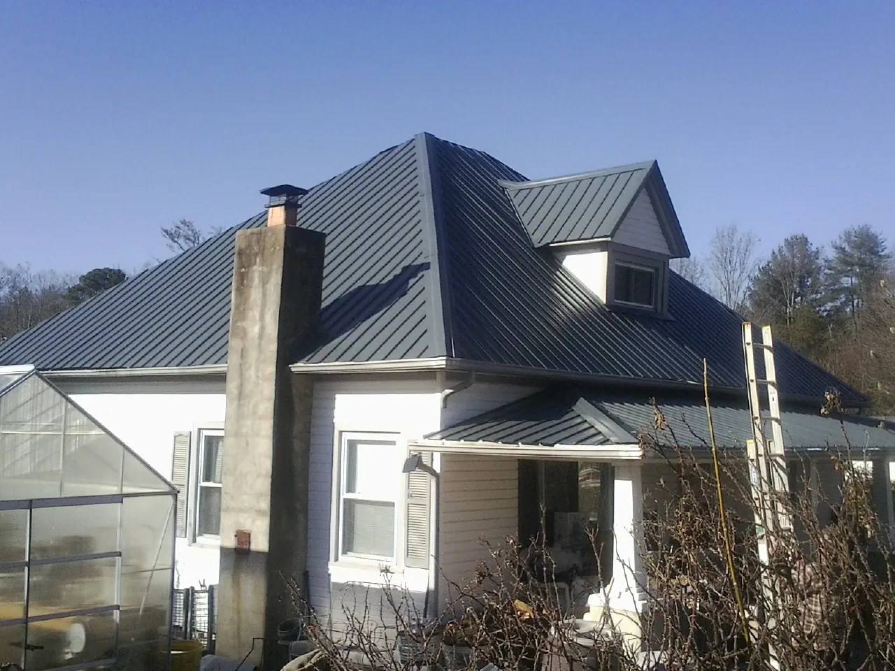 Dark blue standing seam metal roof on a white farmhouse with dormer — Slate & Tile Roof Repair by Roofing Brothers in Topeka