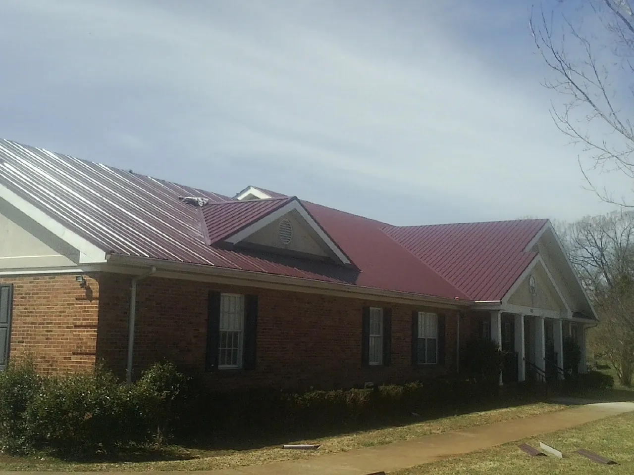 Red metal roof with gabled entries on a long brick building, from a Hail Damage Roof Repair job in Topeka