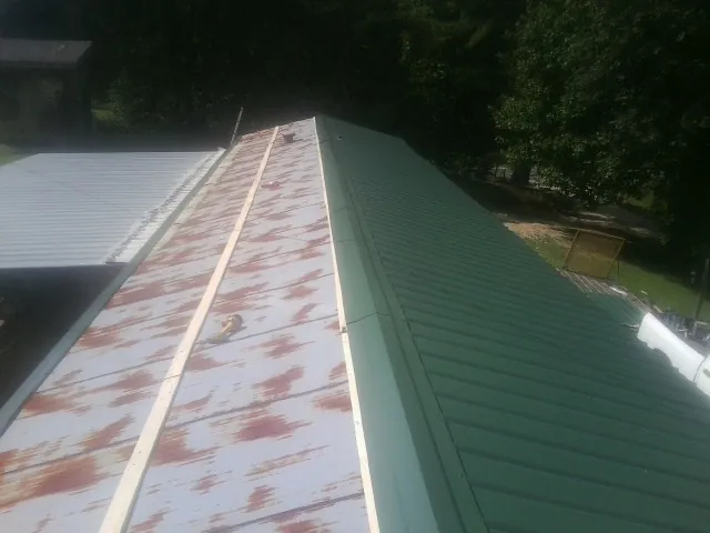 Old rusted panels beside newly installed green metal roofing — Wind Damage Roof Repair by Roofing Brothers in Topeka